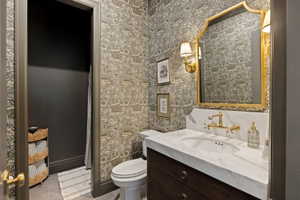 Bathroom with decorative wallpaper, a dark wood-finish vanity, and a wall-mounted brass faucet