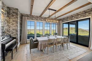 Dining area featuring wood-finish flooring, exposed ceiling beams, and decorative wall covering