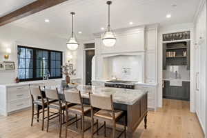 Gourmet kitchen featuring a large central island with seating, a professional-grade range with pot filler, custom white cabinetry, and light wood-finish flooring