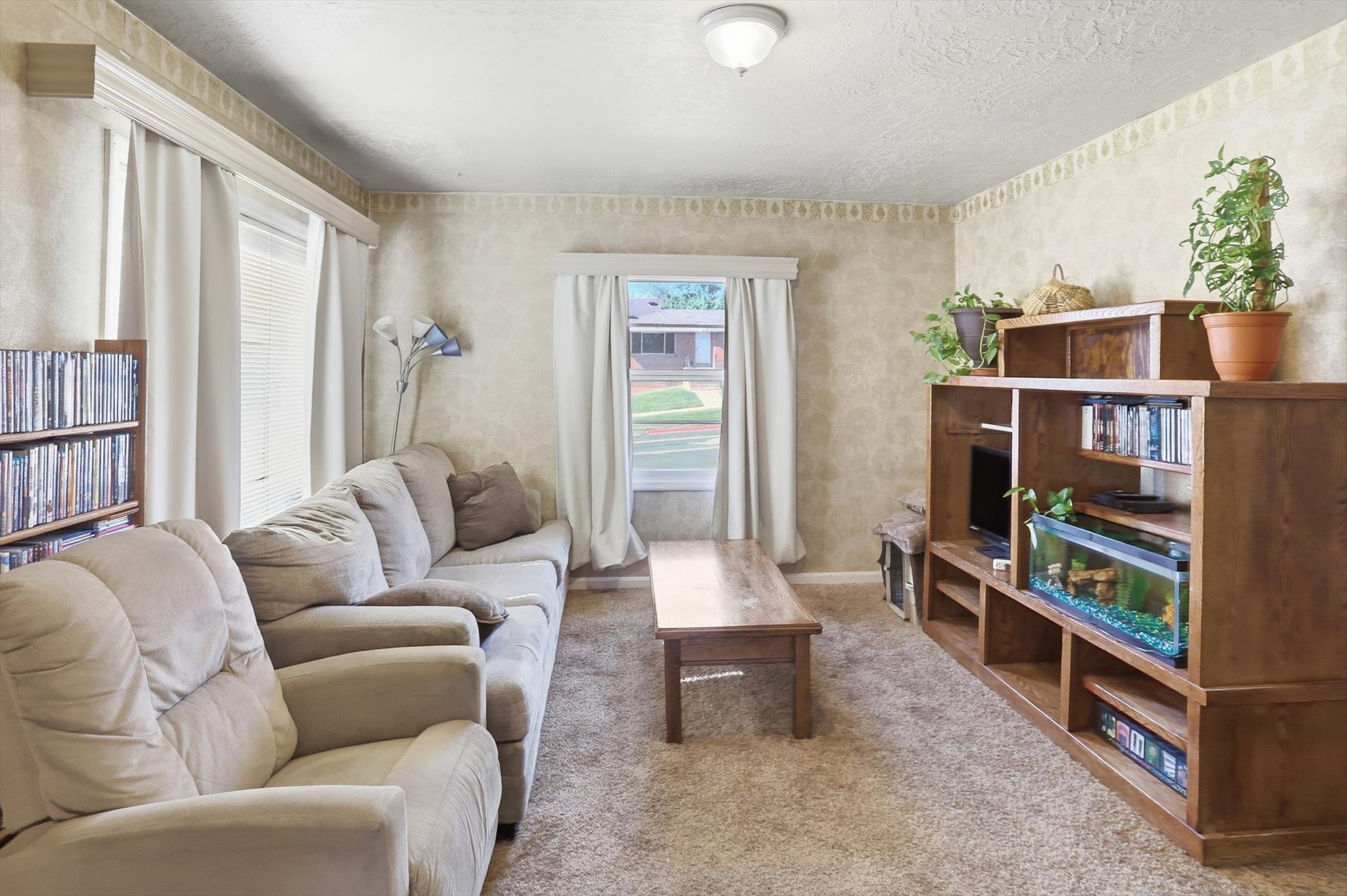 Living area featuring textured wallpaper, carpet flooring, a flush-mount ceiling light, and a built-in media center with shelving