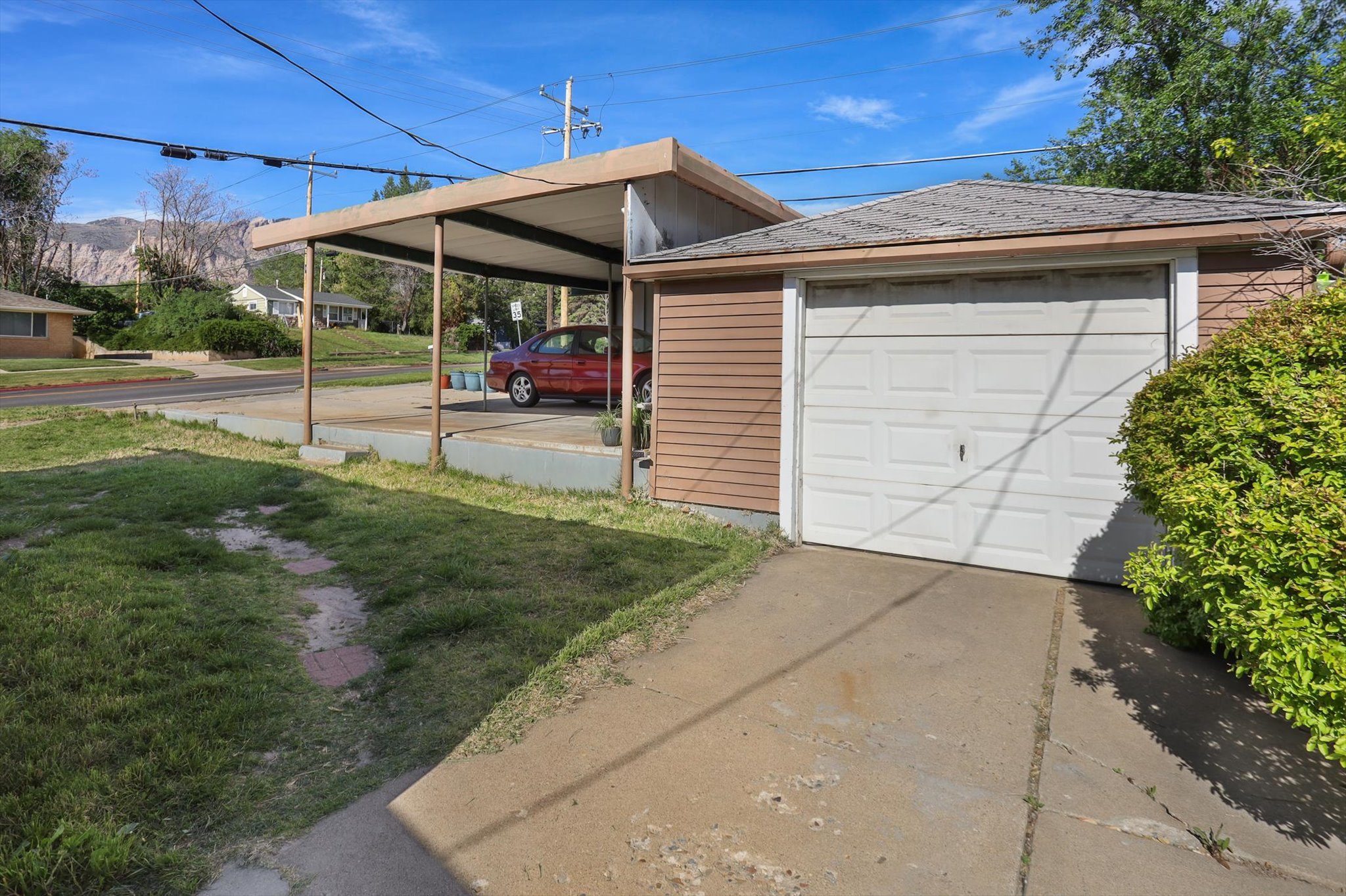 Detached garage with a single panel door, a concrete driveway, and an attached carport with metal supports
