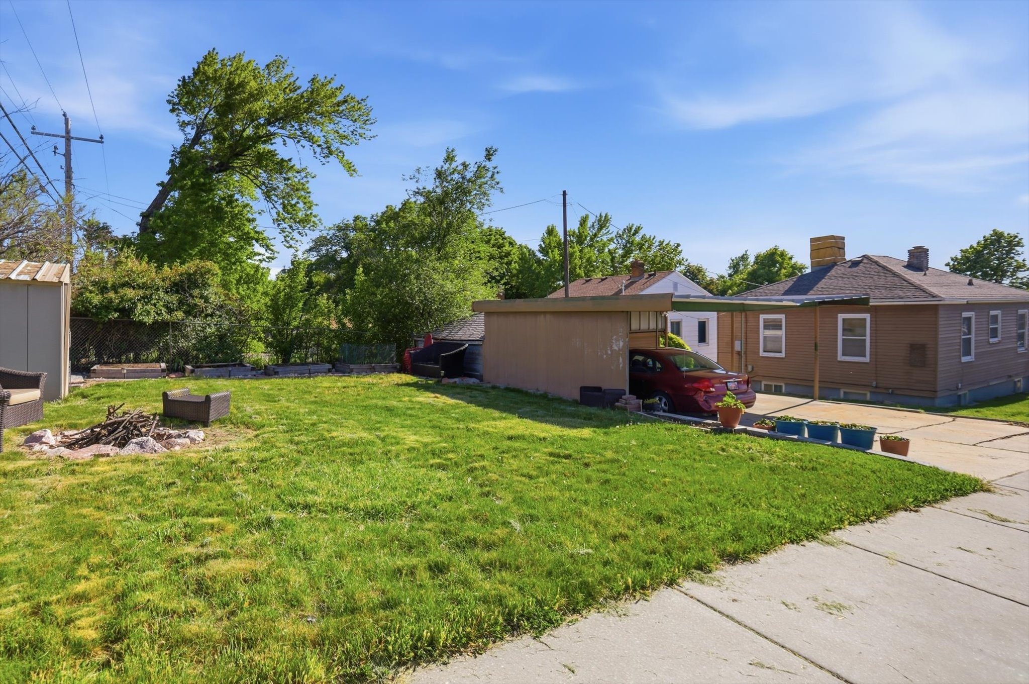Expansive grassy yard area featuring a fire pit, mature perimeter trees, and a storage shed