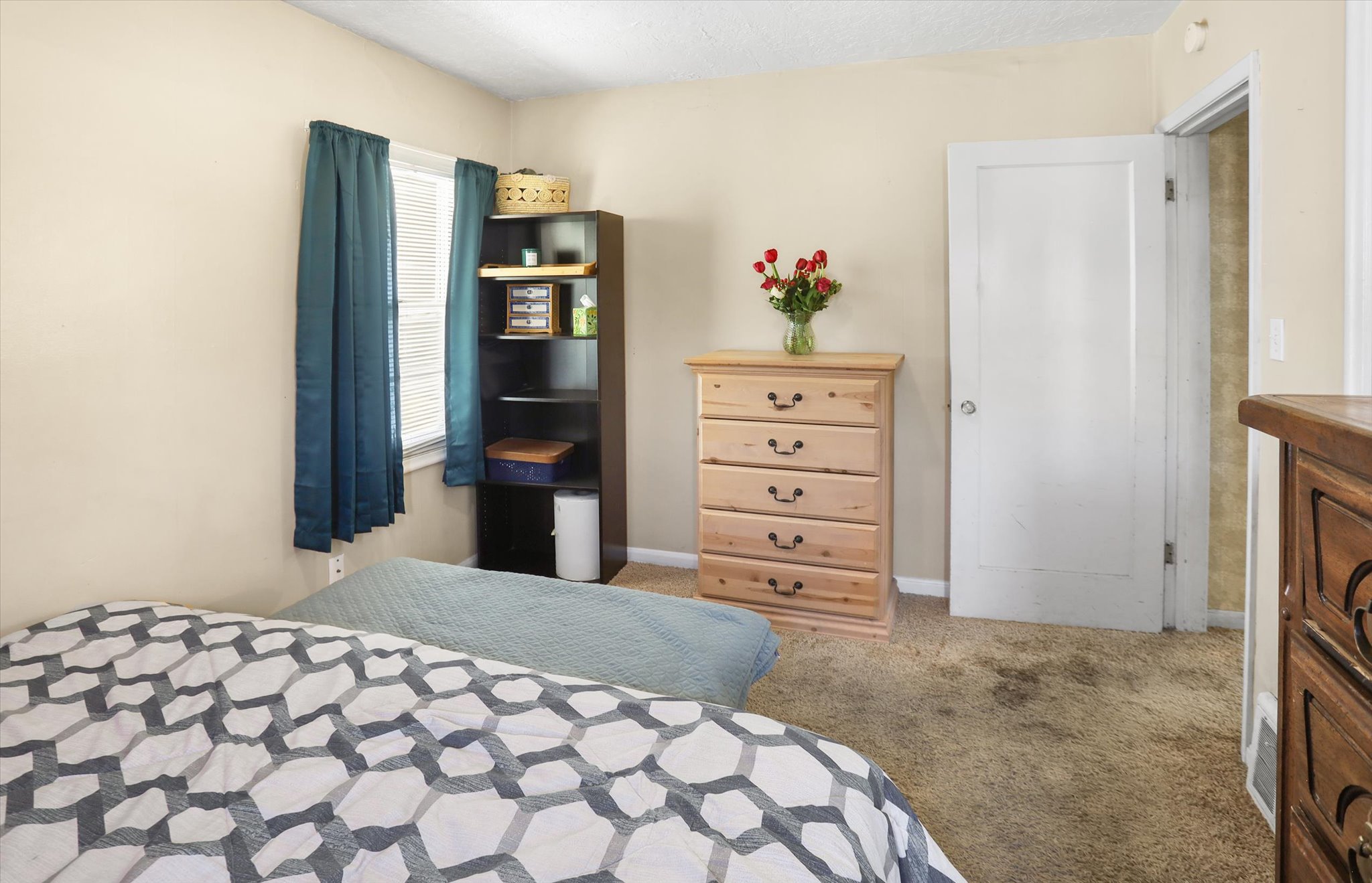 Carpeted room with a single window featuring blinds and blue drapes