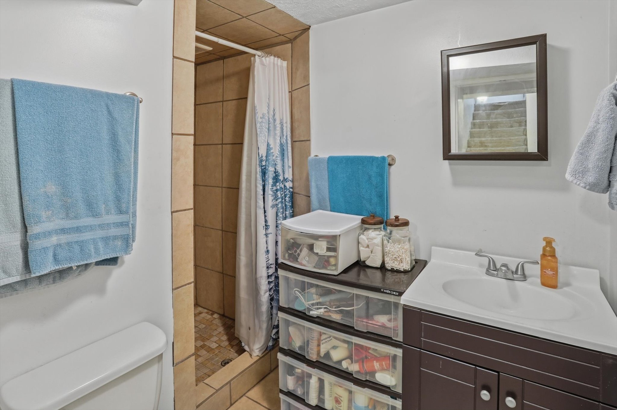 Bathroom featuring a tile shower with a mosaic floor, a white vanity with an integrated sink, a dark wood-finish cabinet, and a wall-mounted mirror