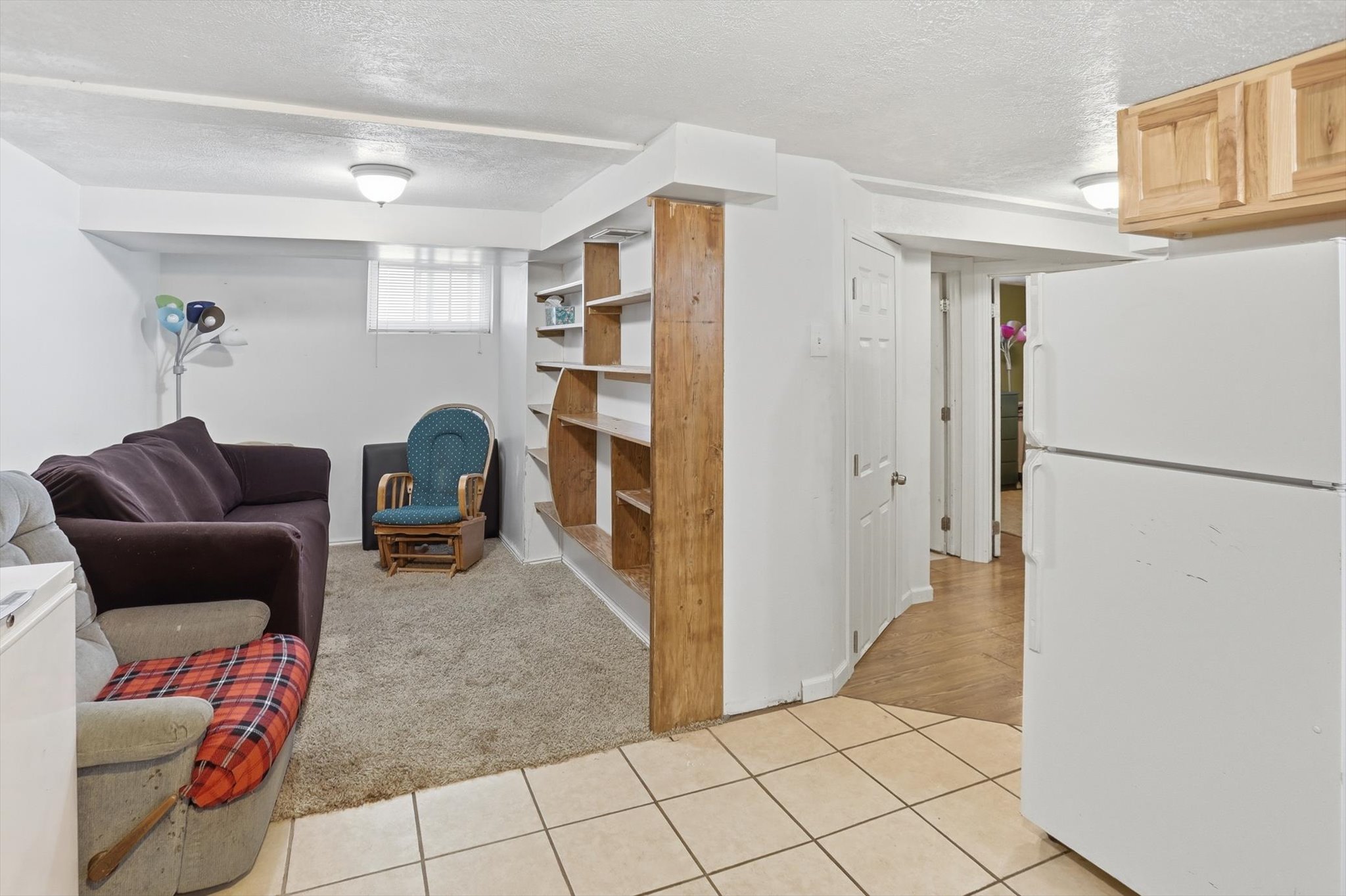 Finished lower-level space featuring ceramic tile and carpet flooring, built-in wooden shelving, and a window with blinds