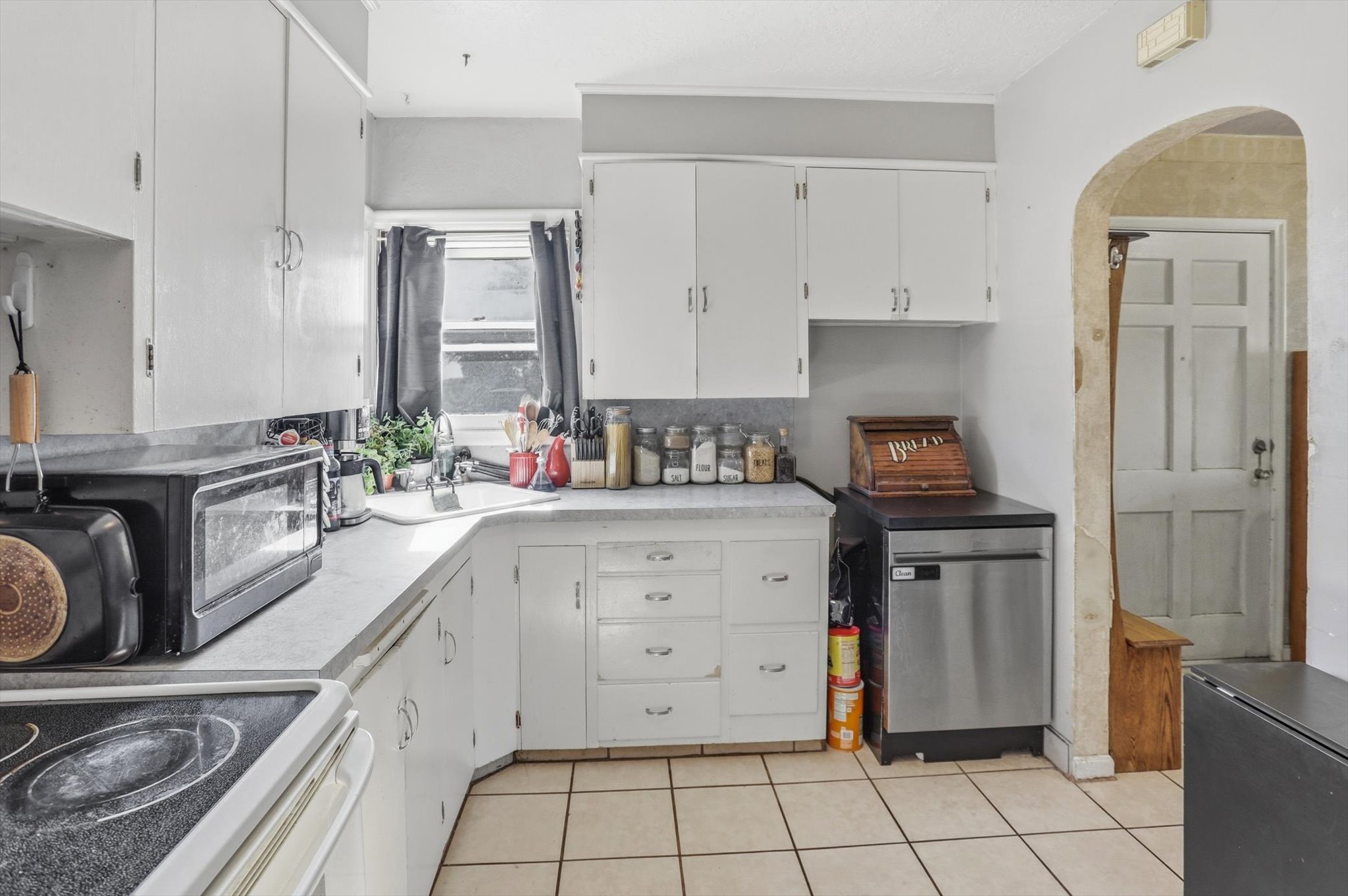 Kitchen featuring white cabinetry, light-toned countertops, a stainless steel dishwasher, and tile flooring