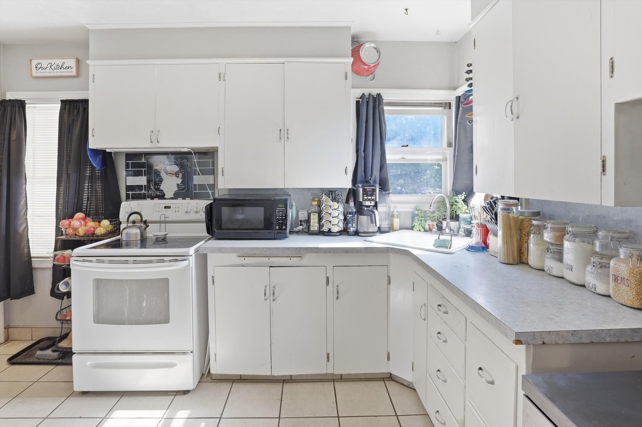 White cabinetry with brushed nickel hardware, L-shaped laminate countertops, tiled backsplash, and ceramic tile flooring