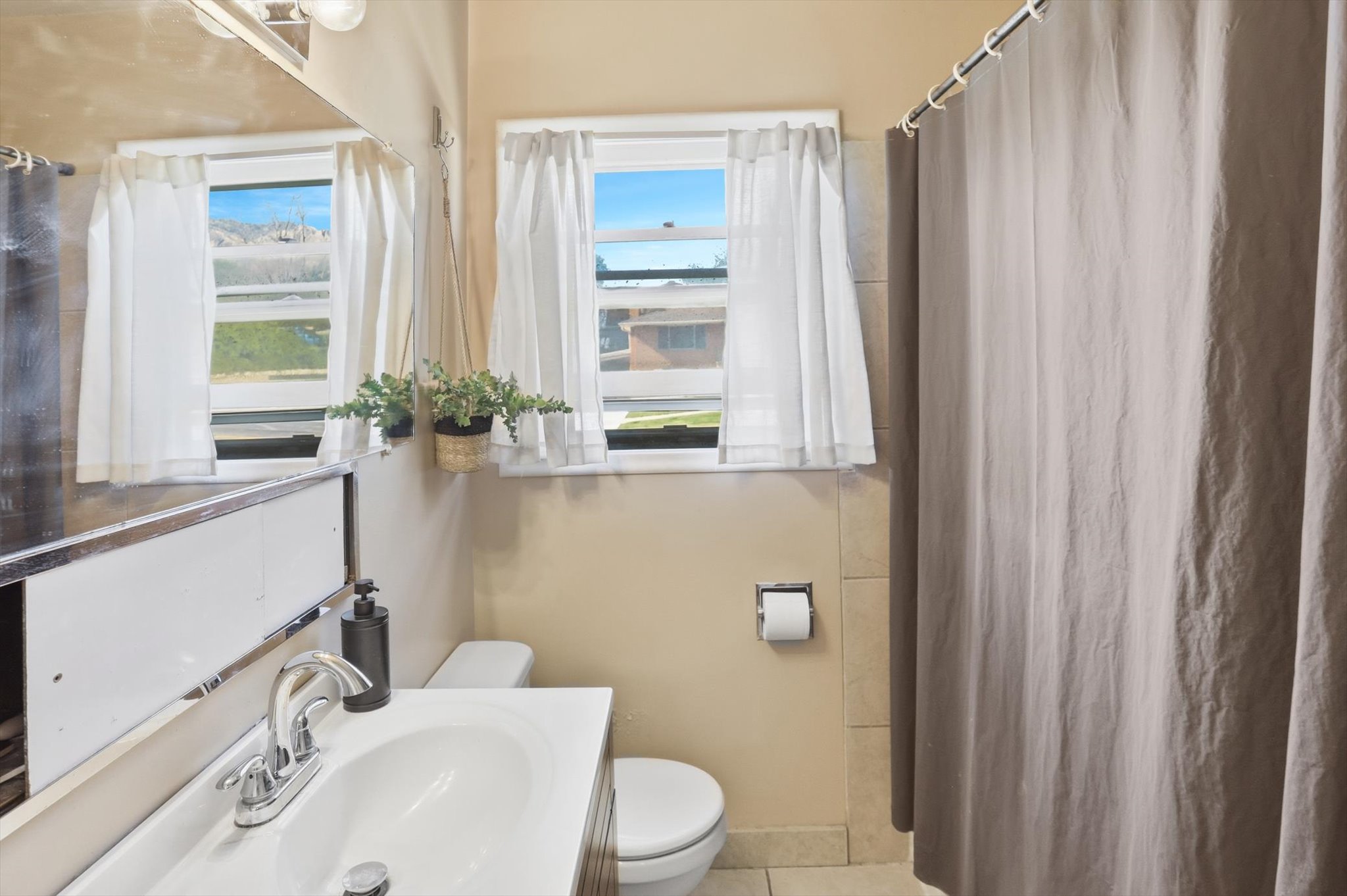 Bathroom featuring a window, tile flooring, a shower curtain, a vanity with an integrated sink, and a toilet