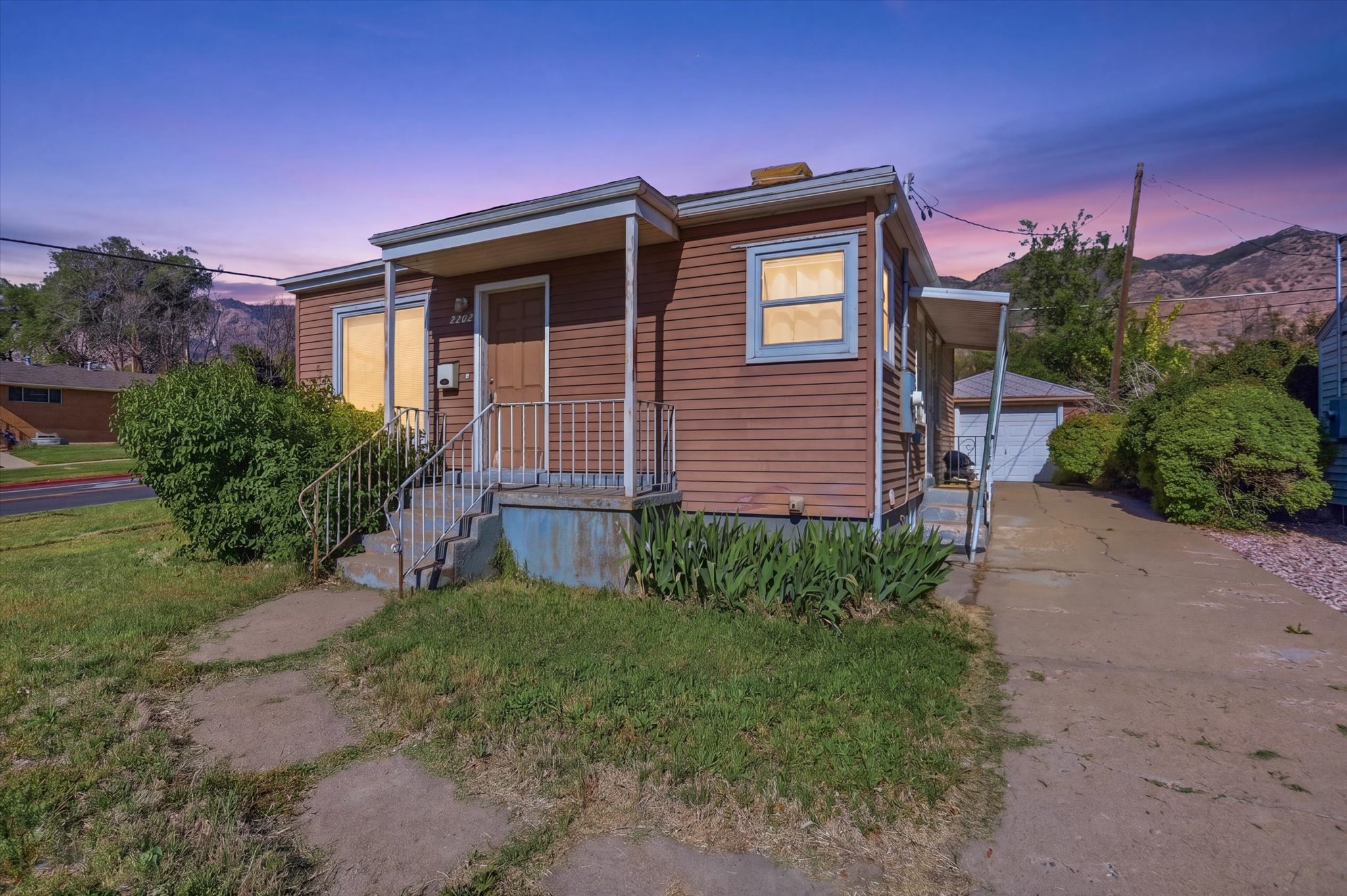 Brown siding exterior with white trim, covered front porch, and concrete steps with metal railings