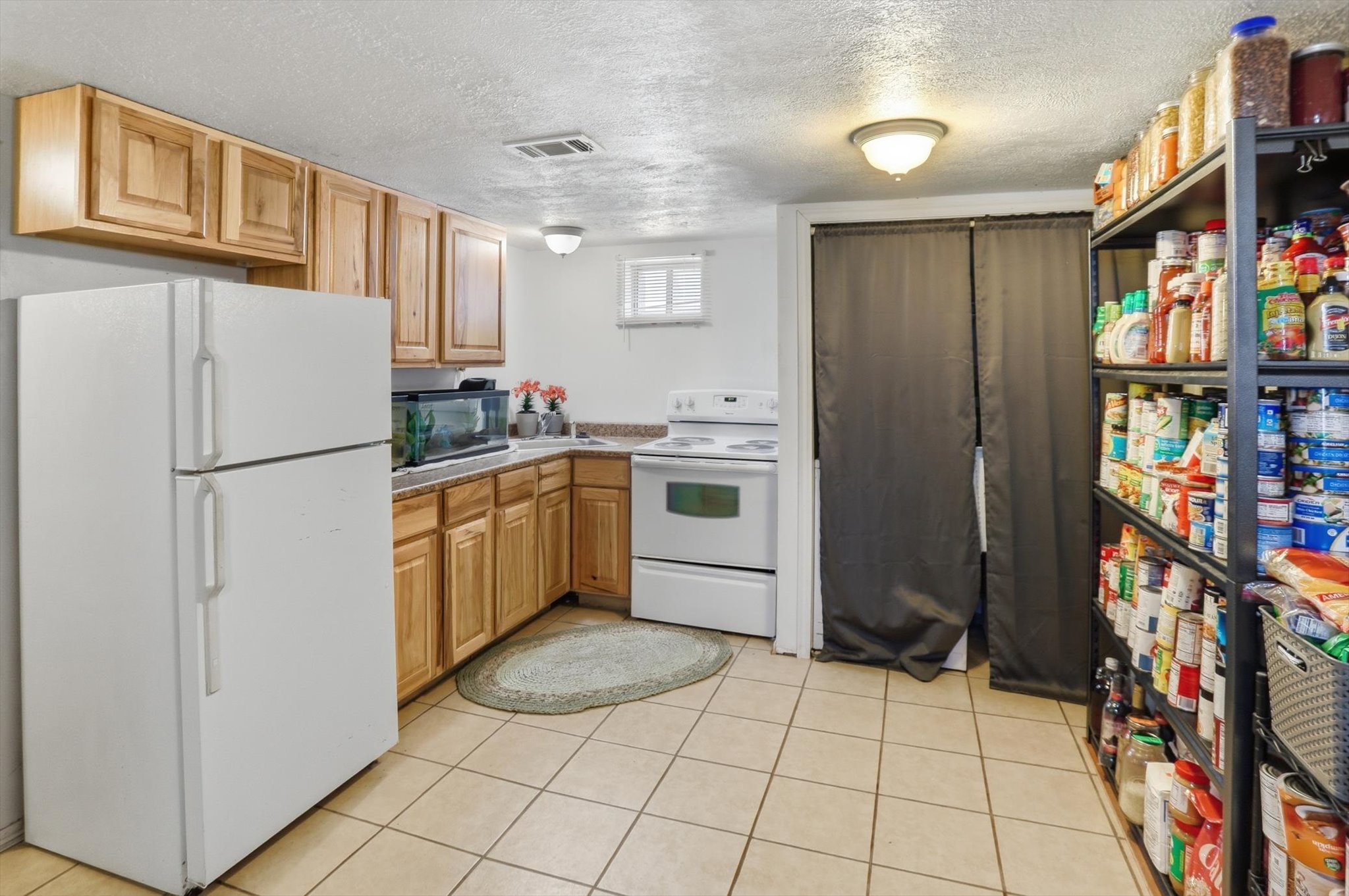 Kitchenette featuring tile flooring, light wood cabinetry, white appliances, and a window for natural light