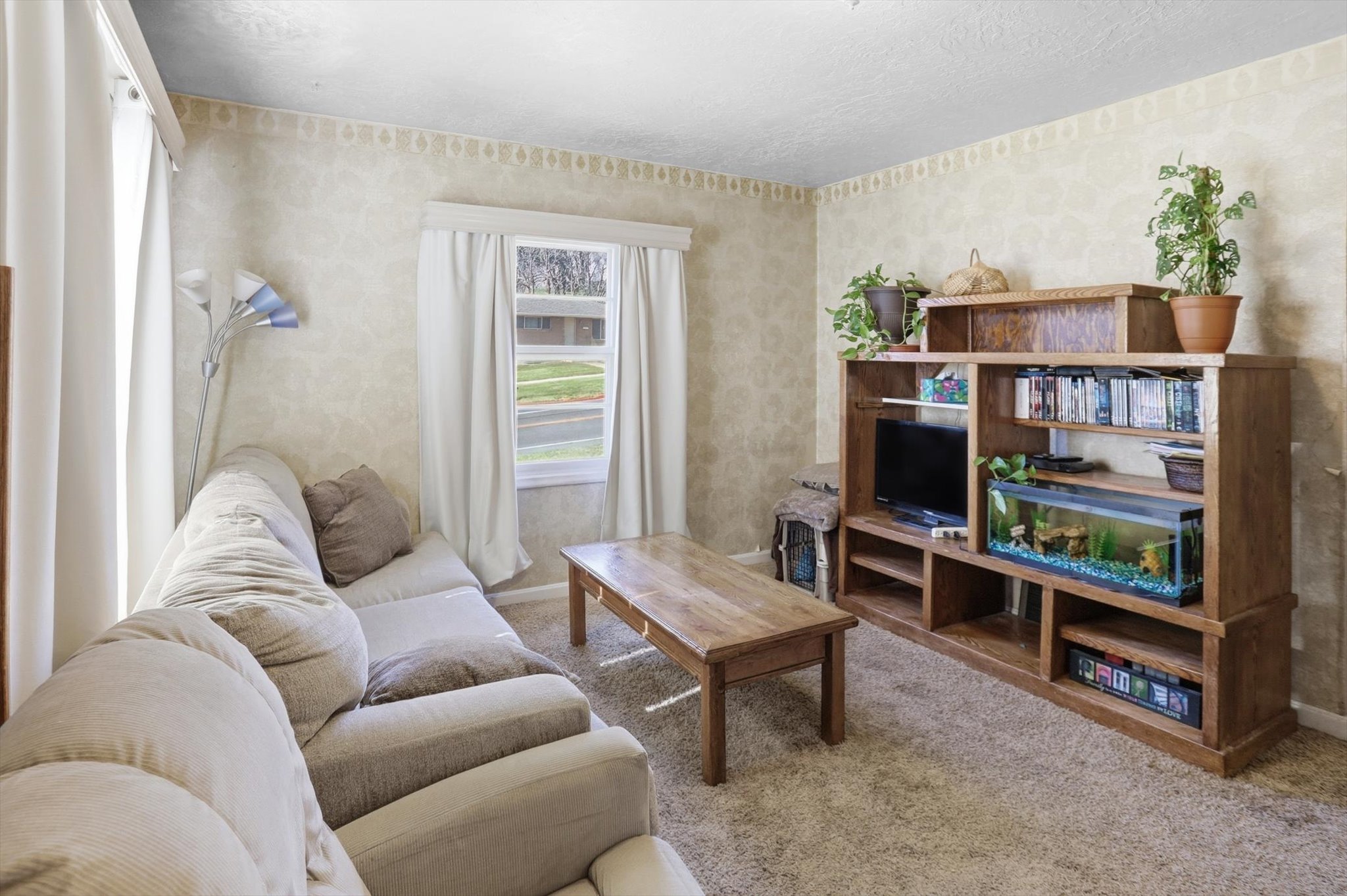 Carpeted living area featuring a single window and textured wallpaper