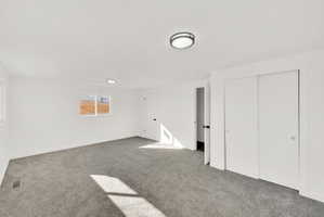 Spacious room featuring neutral carpet, white walls, two windows, two flush-mount ceiling lights, and white sliding closet doors