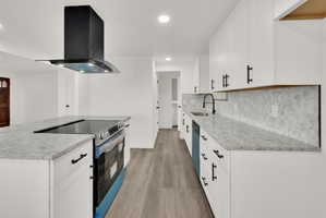 Kitchen featuring white cabinetry, light-toned countertops, a geometric tile backsplash, a built-in electric cooktop, and a black range hood