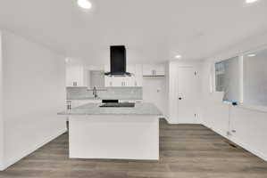 Contemporary kitchen featuring an island with an integrated cooktop, white cabinetry, and a black range hood