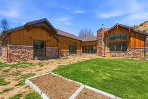 Spacious backyard featuring a manicured lawn, an elevated garden bed, a stone and wood-clad exterior, a stone chimney, and large windows