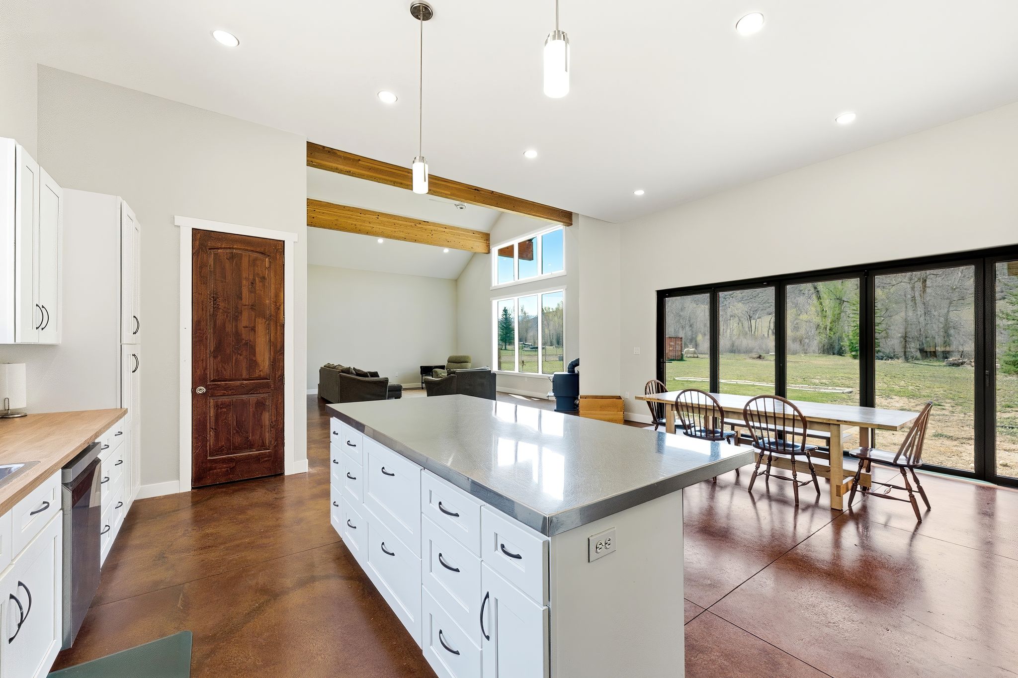 Expansive open-concept living space featuring a large kitchen island with a light-toned countertop, white cabinetry with black hardware, and concrete-finish flooring