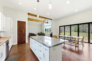 Expansive open-concept living space featuring a large kitchen island with a light-toned countertop, white cabinetry with black hardware, and concrete-finish flooring