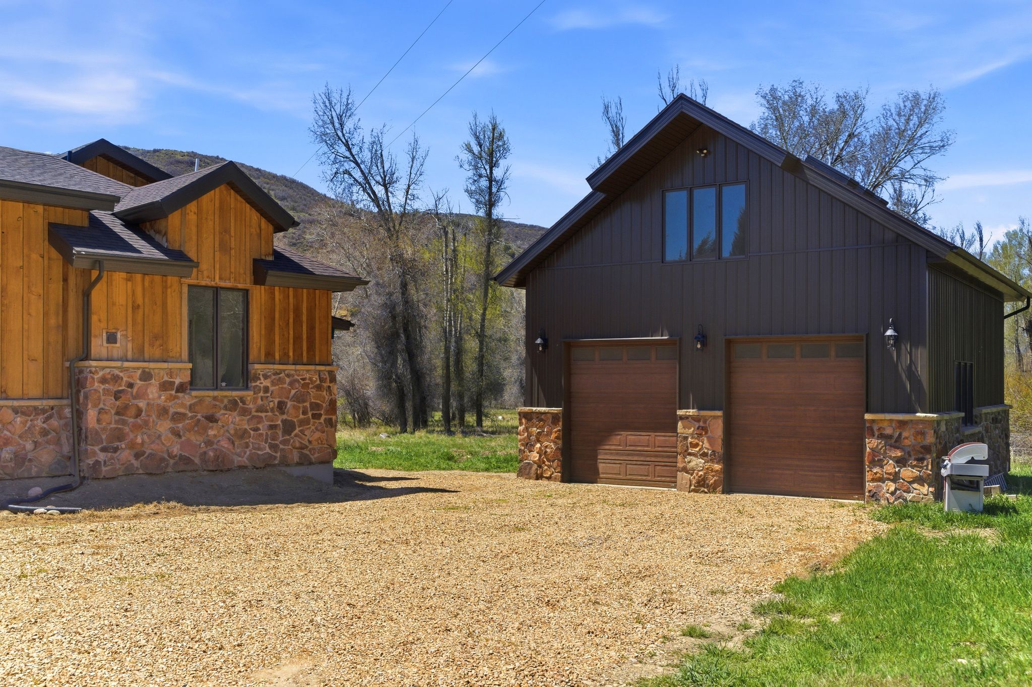 Detached auxiliary building with two wood-finish garage doors, board and batten siding, and stone accents