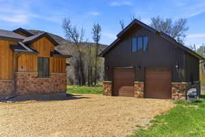 Detached auxiliary building with two wood-finish garage doors, board and batten siding, and stone accents