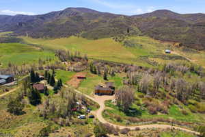 Expansive rural property featuring multiple structures, verdant hillsides, mature trees, and a winding dirt road
