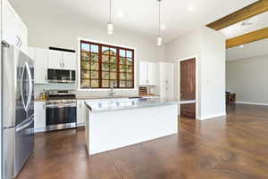 Kitchen featuring a large window, white cabinetry, stainless steel appliances, a center island with a metallic countertop, and high ceilings with exposed wood beams