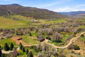 Expansive mountain valley property featuring multiple structures, verdant fields, a dirt road, and abundant mature trees
