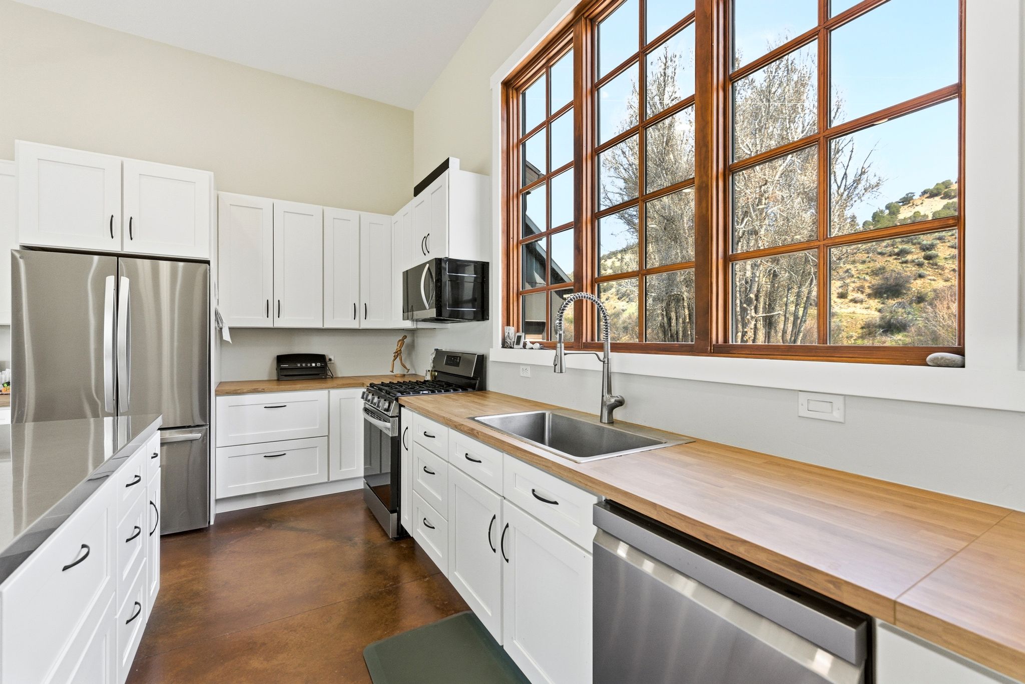 Kitchen featuring white shaker cabinetry, wood-finish countertops, stainless steel appliances, and a large multi-pane window with wood-finish trim