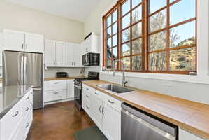 Kitchen featuring white shaker cabinetry, wood-finish countertops, stainless steel appliances, and a large multi-pane window with wood-finish trim