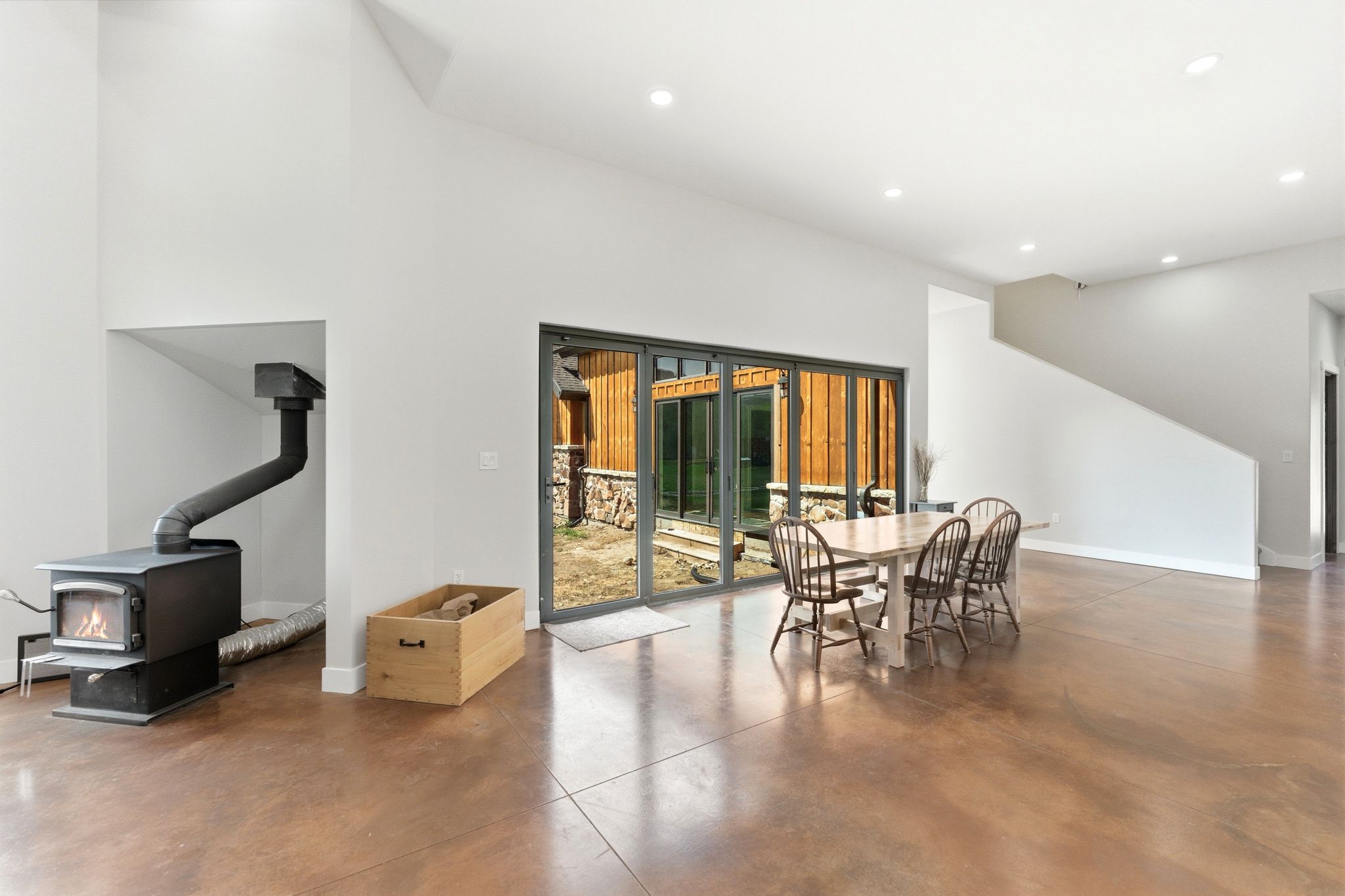 Open-concept living space featuring vaulted ceilings, a built-in wood-burning stove, stained concrete flooring, and a sliding glass door system