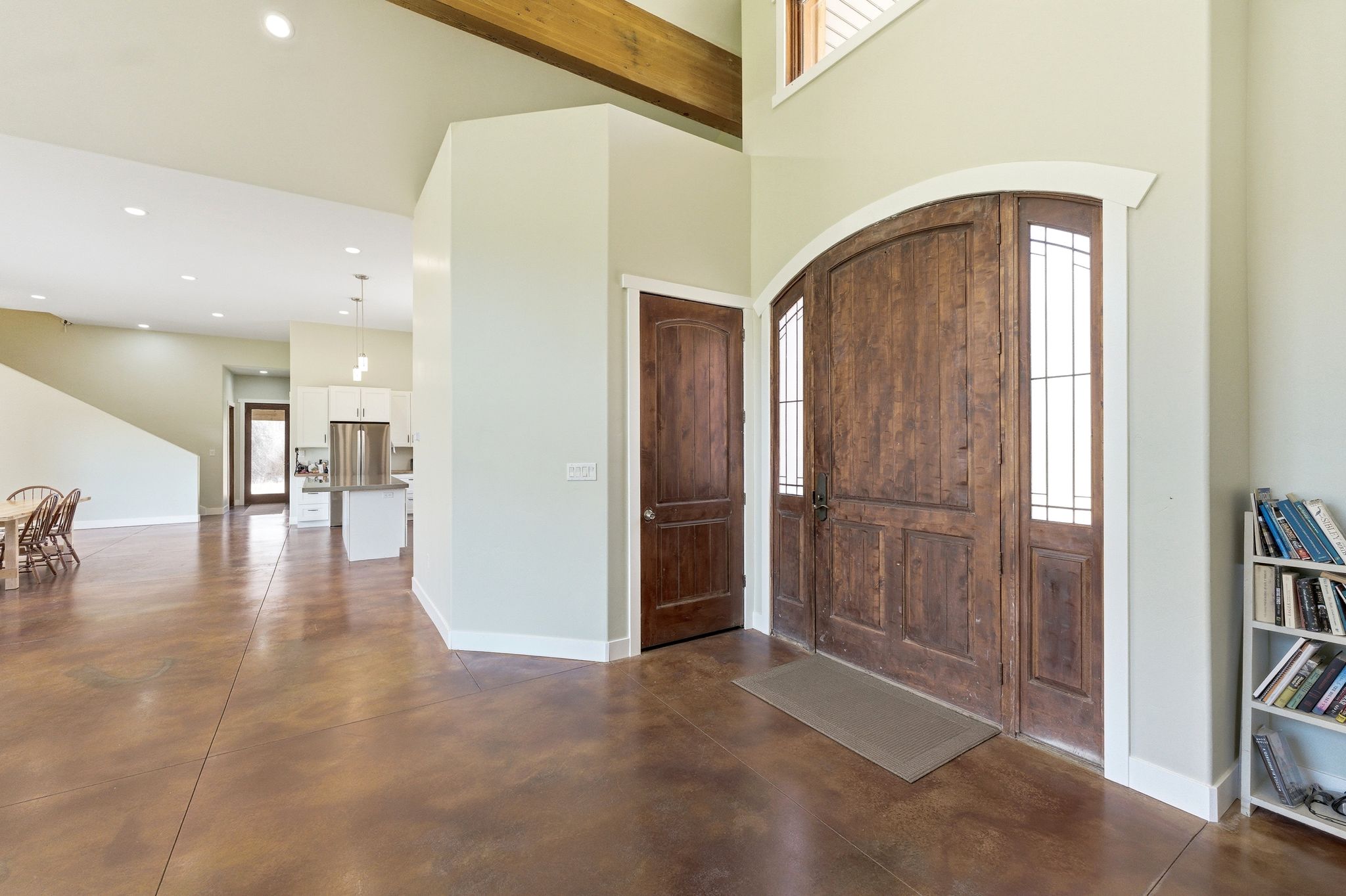 Grand entry featuring a tall vaulted ceiling, exposed wood beam, arched double entry doors with sidelights, and durable concrete flooring