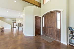 Grand entry featuring a tall vaulted ceiling, exposed wood beam, arched double entry doors with sidelights, and durable concrete flooring