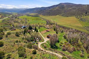 Expansive rural landscape featuring a winding dirt road, multiple structures, and varied topography including rolling hills and mountainous terrain