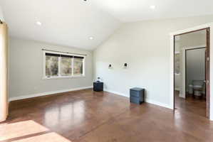 Vaulted ceiling room with stained concrete flooring, recessed lighting, wall-mounted sconces, and a large window overlooking natural scenery