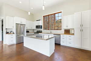 Spacious kitchen featuring an expansive island with a stainless steel countertop, white cabinetry with black hardware, stainless steel appliances, wood-finish countertops, and large windows