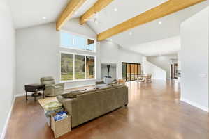 Expansive living area featuring vaulted ceilings with exposed wood beams, large picture windows, recessed lighting, and polished concrete flooring