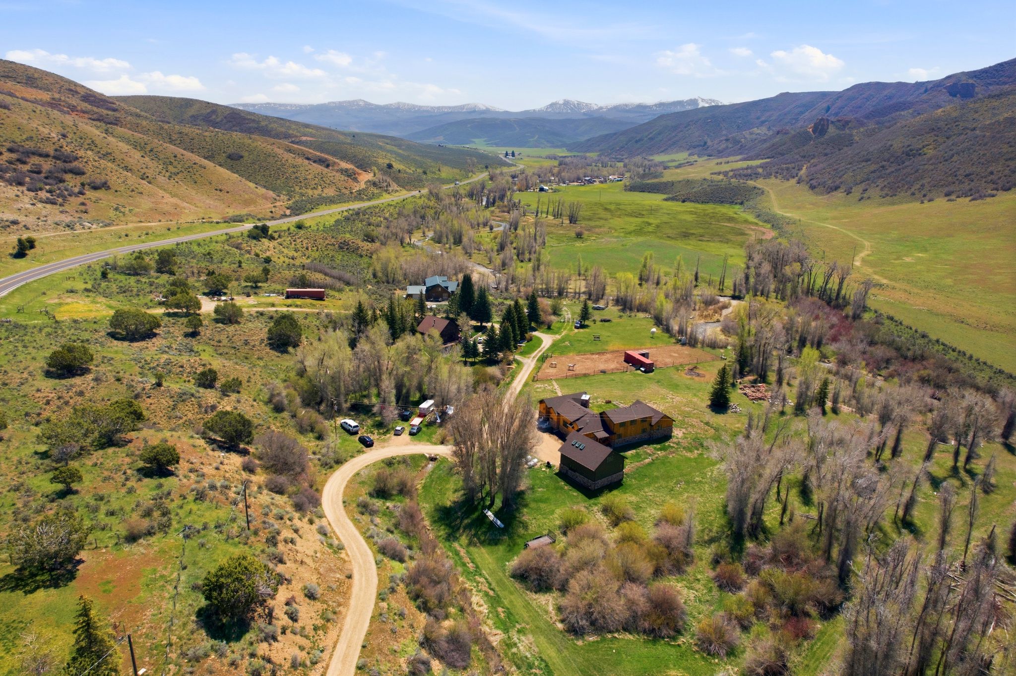 Expansive property featuring multiple structures, including a primary residence with multi-level roofing, situated within a verdant valley
