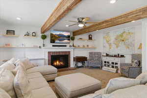 Spacious living area featuring exposed wood beams, recessed lighting, and a brick-surround fireplace with a white mantel