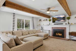 Living area featuring a brick-surround fireplace with a white mantel, ceiling fan, recessed lighting, wood-finish ceiling beams, and sliding glass doors