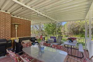 Expansive covered deck featuring a brick exterior wall, a white railing system, and a corrugated metal roof with integrated lighting