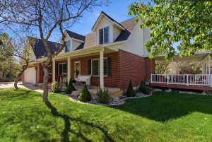 Brick and siding exterior featuring a covered front porch, white garage door, dormer windows, and established landscaping