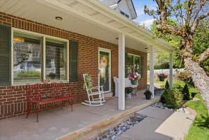 Brick facade featuring dark green shutters, a covered front porch, white columns, and a concrete pathway