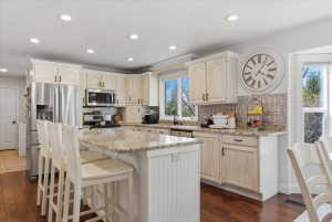 Kitchen featuring a central island with a granite countertop, recessed lighting, wood-finish flooring, white cabinetry, and stainless steel appliances