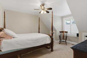 Carpeted room featuring a ceiling fan with integrated lighting, a window with white plantation shutters, and a sloped ceiling design
