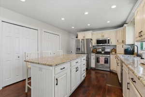 Spacious kitchen featuring a large central island with seating, extensive countertop space, cream-colored cabinetry, stainless steel appliances, and dark wood-finish flooring