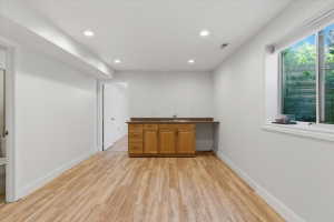 Spacious room featuring wood-finish flooring, recessed lighting, and a built-in wet bar with wooden cabinetry and a stone-finish countertop