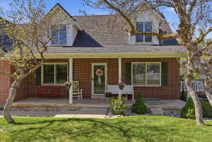 Brick facade residence featuring a covered front porch, white-framed windows with dark shutters, and a dormer window on the upper level