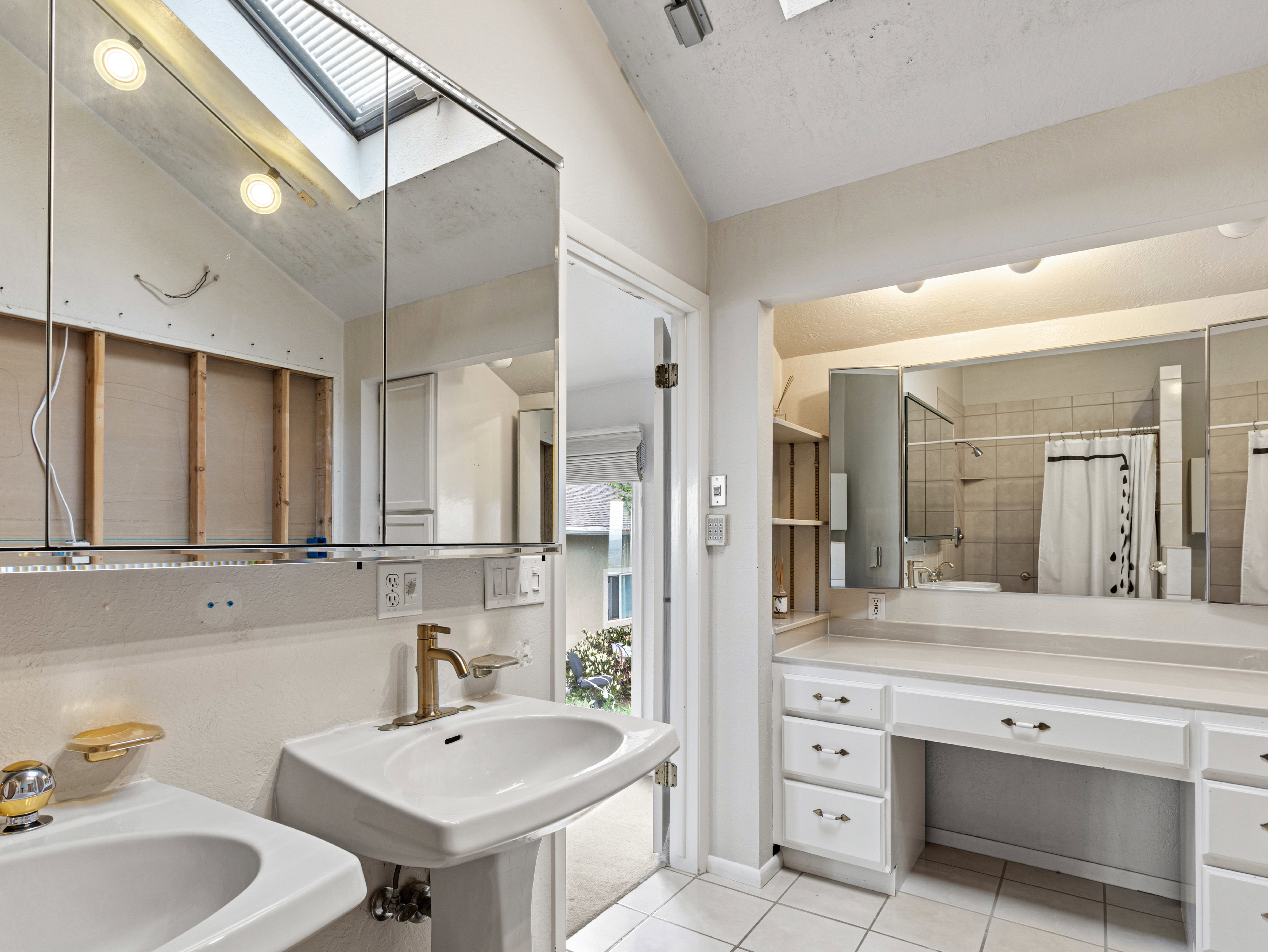 Bathroom featuring a skylight, dual pedestal sinks, a vanity area with built-in cabinetry, and tile flooring