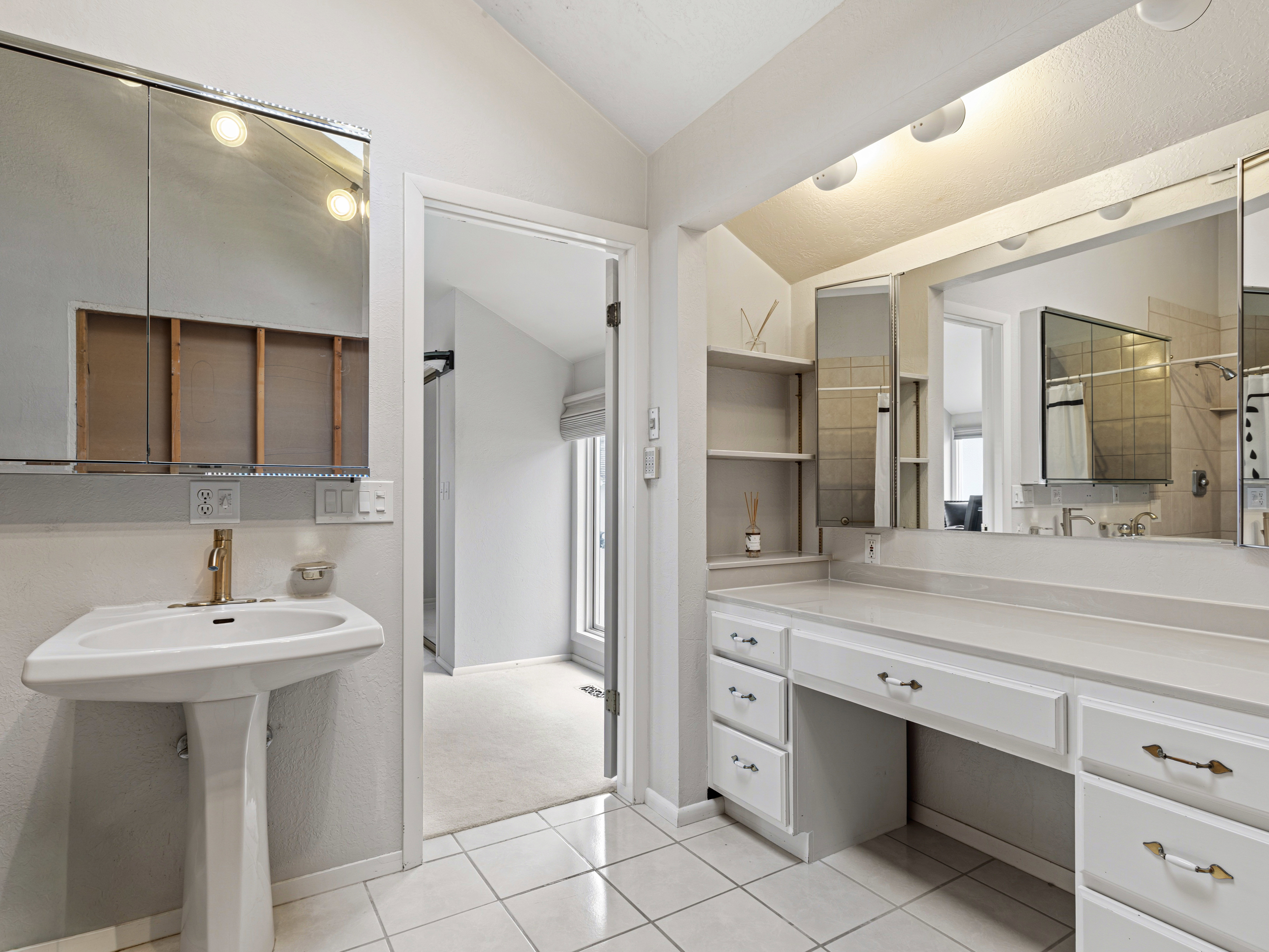 White tiled flooring with a pedestal sink, brass-finish faucet, and a wall-mounted mirrored medicine cabinet