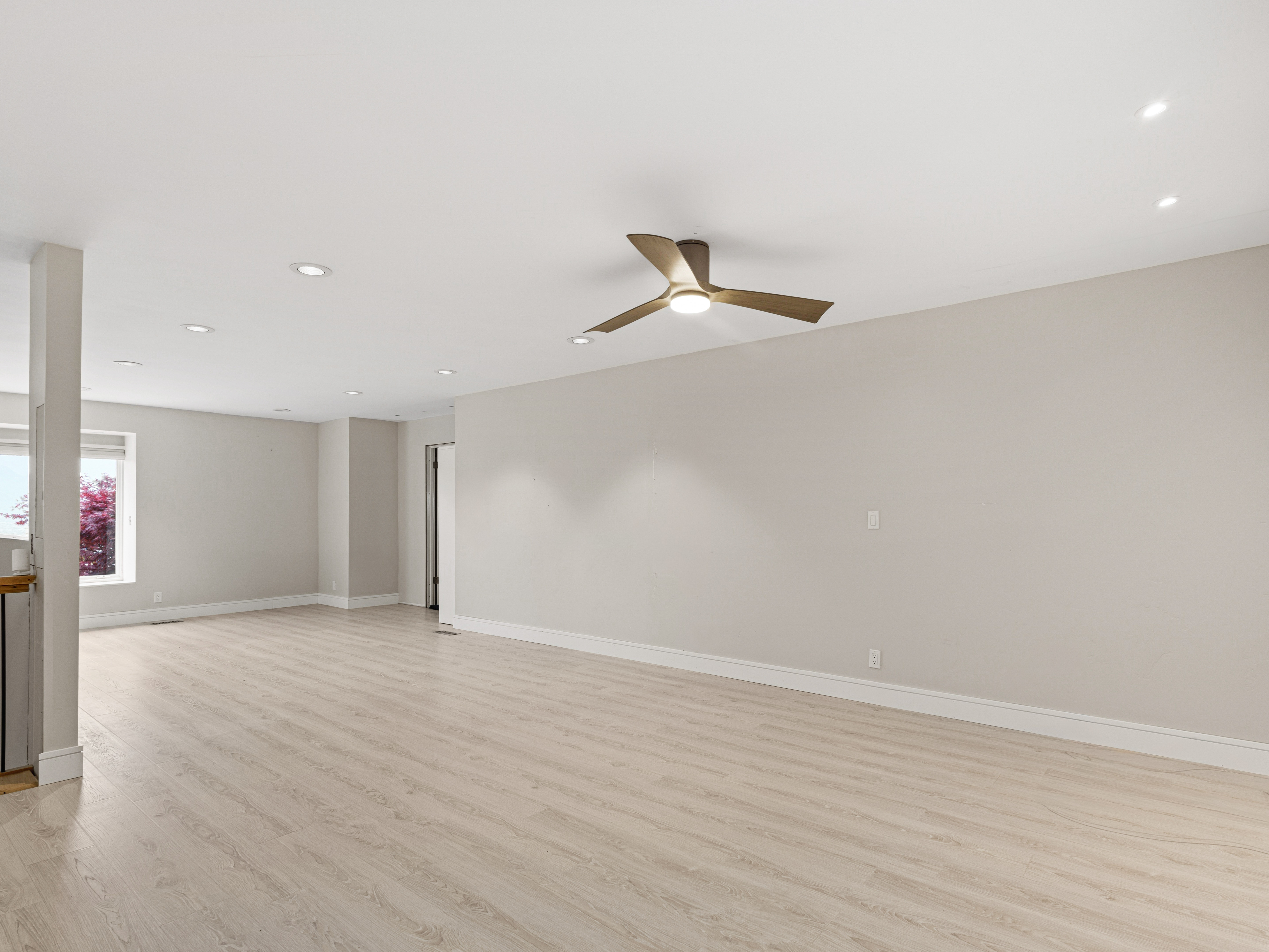 Spacious room with light wood-finish flooring, recessed lighting, and a modern ceiling fan