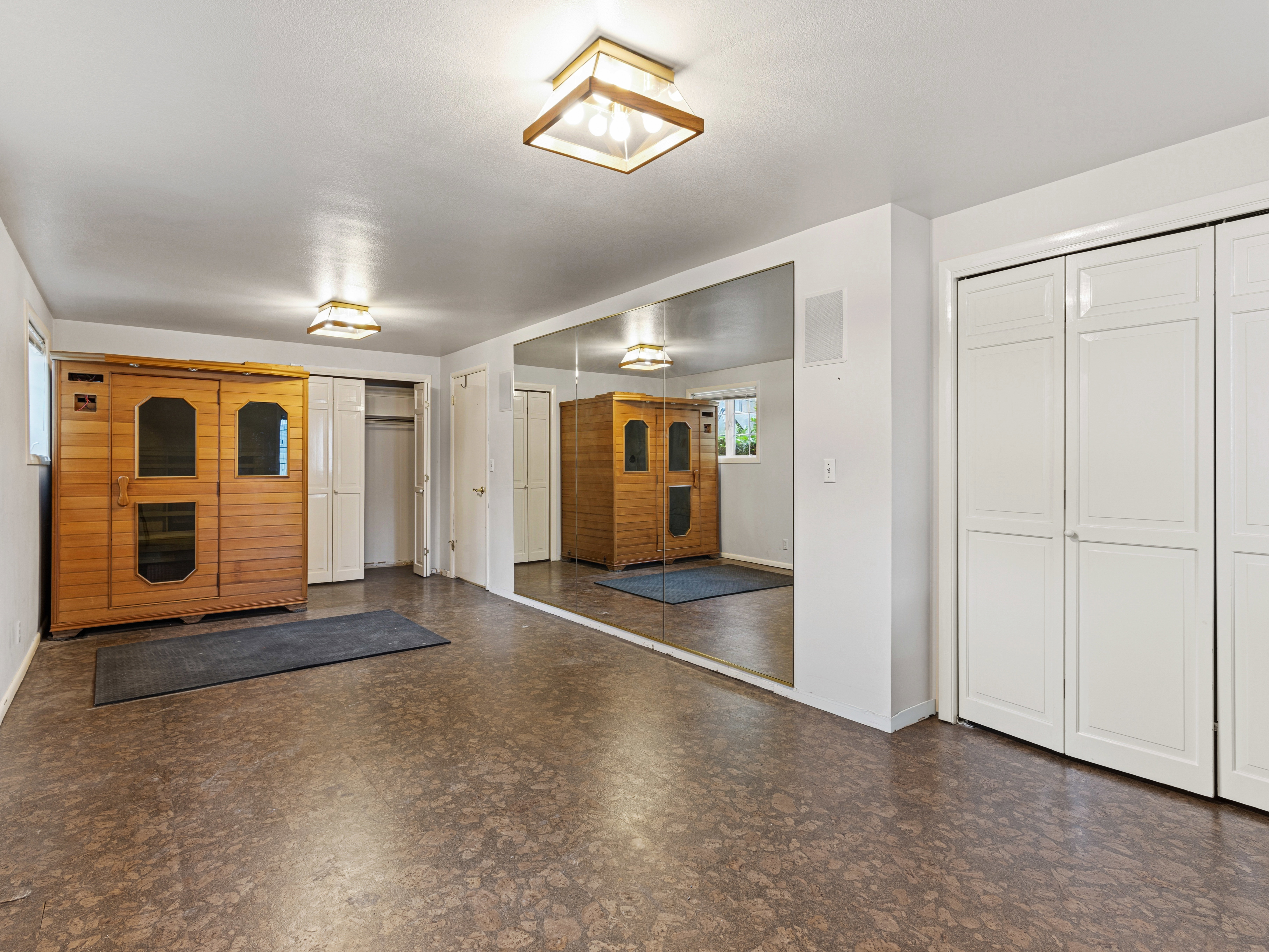 Recreation room with full-wall mirror, two sets of bi-fold closet doors, and recessed lighting